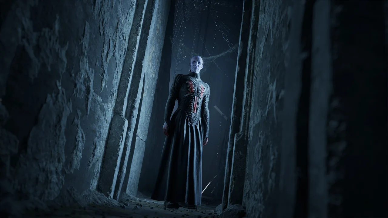 A pale figure in a long dark coat, the head studded with pins, standing in a carved stone passage